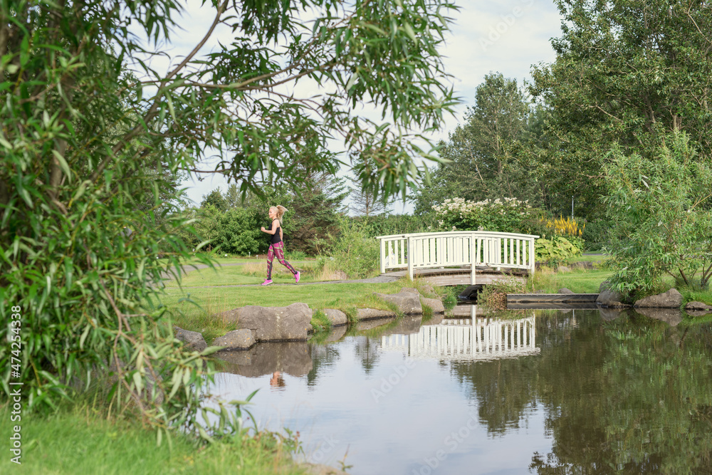 Unrecognizable lady jogging near pond in park Unrecognizable lady jogging near pond in park