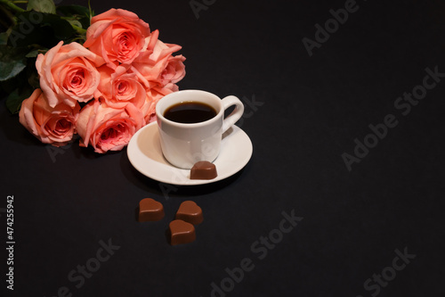 Cup of coffee, heart shape chocolate candies and pink roses.