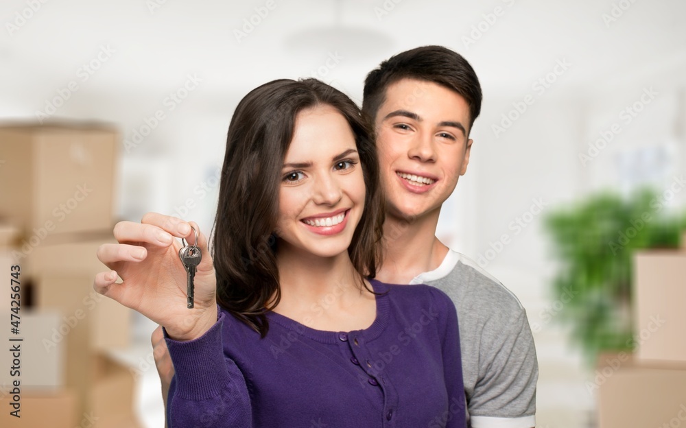 Cheerful lady, showing house key indoors. Lovely couple posing in new apartment