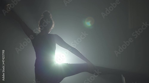 Woman dancer from behind stretching her leg with backlight