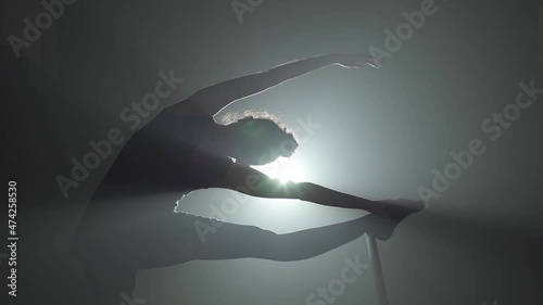 Woman dancer from behind stretching her leg with backlight
