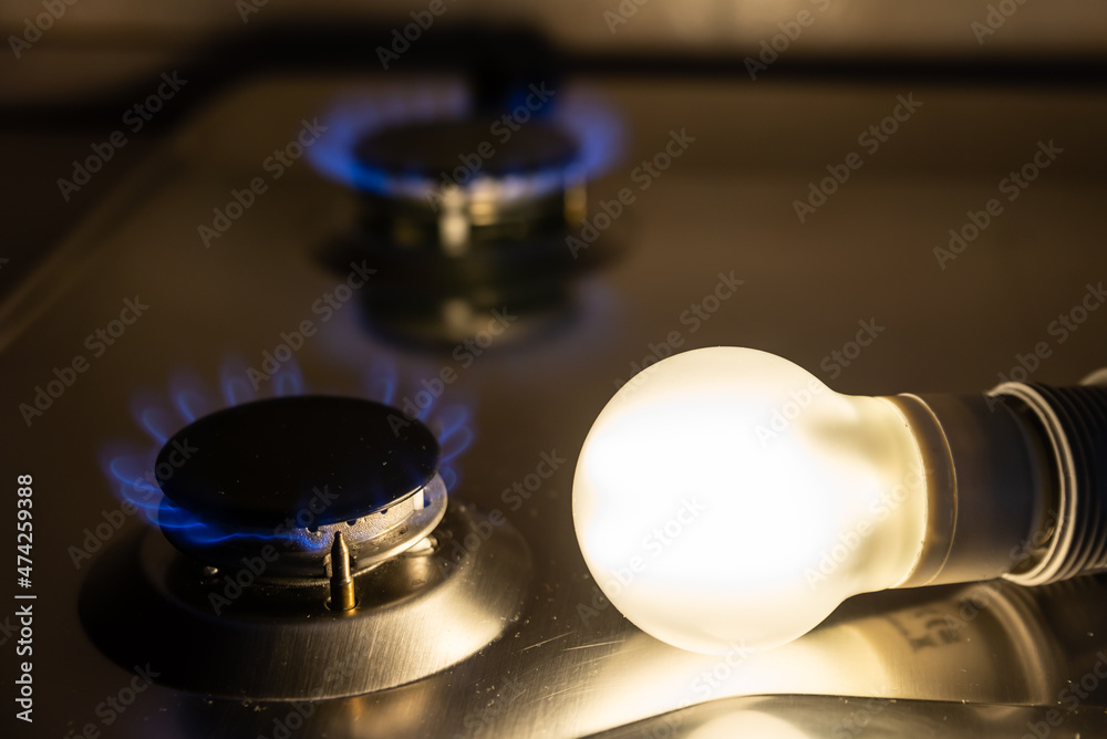 Light bulb on next to lit gas cooker, with coins next to it. Energy and gas costs, cost increases. Light bulb on next to lit gas cooker, with coins next to it. Energy and gas costs, cost increases.
