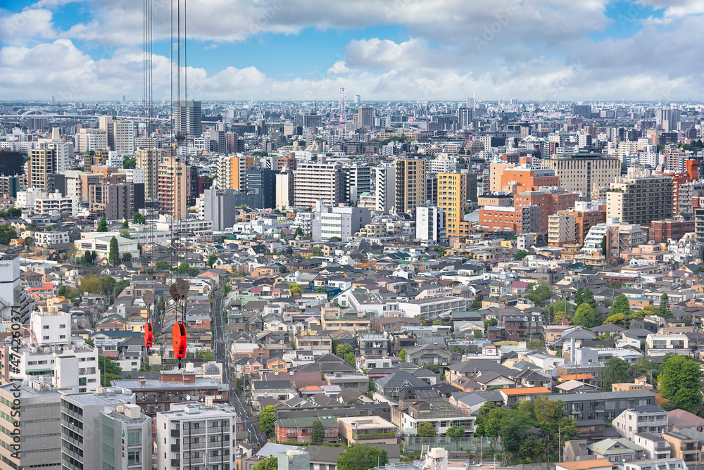 Hook block and wire rope of an electric elevated crane used for construction hung above a cityscape of Tokyo city with skyscrapers, buildings and clouds on the skyline.