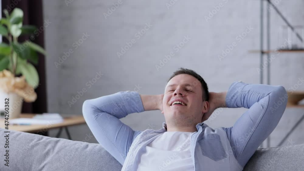 Happy Caucasian man resting on comfortable couch hold hands behind head eyes closed. Slow motion. Handsome young male on sofa at home enjoy stress free. Relaxed man takes break to relieve stress. Happy Caucasian man resting on comfortable couch hold hands behind head eyes closed. Slow motion. Handsome young male on sofa at home enjoy stress free. Relaxed man takes break to relieve stress.