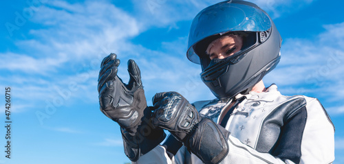 woman dressed as a biker with black safety helmet putting on her leather gloves getting ready to ride a motorcycle