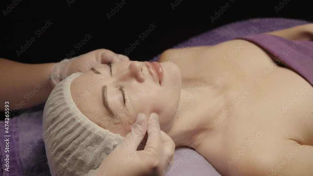 Woman receiving facial massage in spa salon on massage table. Wellness body and skin care, face beauty treatment, receiving rejuvenation procedure Woman receiving facial massage in spa salon on massage table. Wellness body and skin care, face beauty treatment, receiving rejuvenation procedure