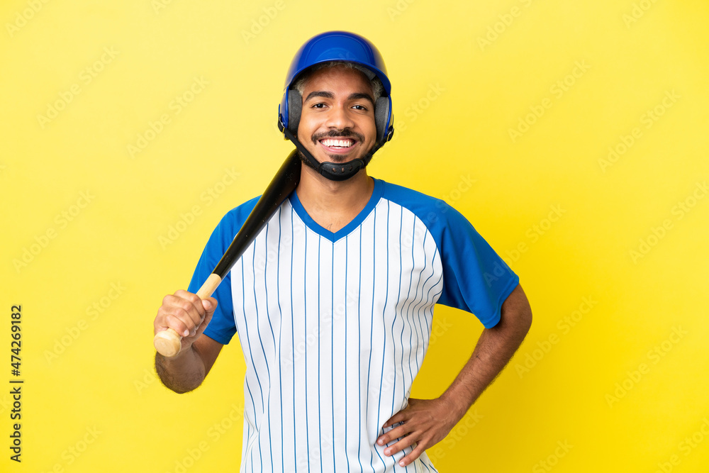Young Colombian latin man playing baseball isolated on yellow background posing with arms at hip and smiling Young Colombian latin man playing baseball isolated on yellow background posing with arms at hip and smiling
