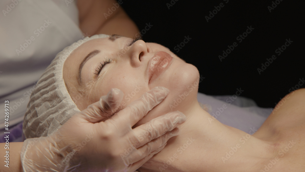 Woman receiving facial massage in spa salon on massage table. Wellness body and skin care, face beauty treatment, receiving rejuvenation procedure Woman receiving facial massage in spa salon on massage table. Wellness body and skin care, face beauty treatment, receiving rejuvenation procedure