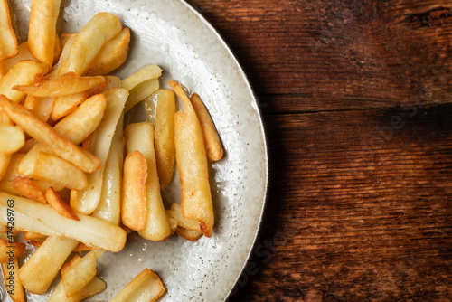 Fried French fries in wedges on a plate on a wooden background.