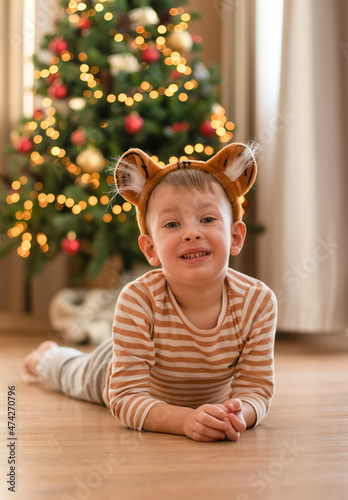 A little boy in a tiger costume lies on the floor against the background of a Christmas tree. Chinese new year symbol