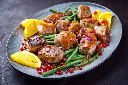 Modern style jusy seared pork pigllet tenderloin fillet meat medallions with orange relish sauce, pomegranate and green baby beans vegetable served as close-up on a Nordic design plate 