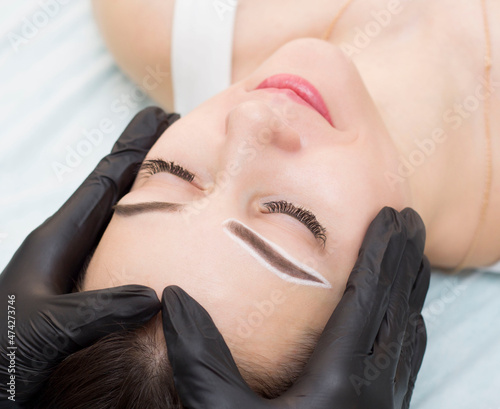 Permanent eyebrow makeup. The master draws a sketch before the permanent makeup procedure with a white pencil.