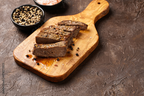A piece of cooked beef meat steak on wooden board cut in slices, white and black peer, coarse sea salt