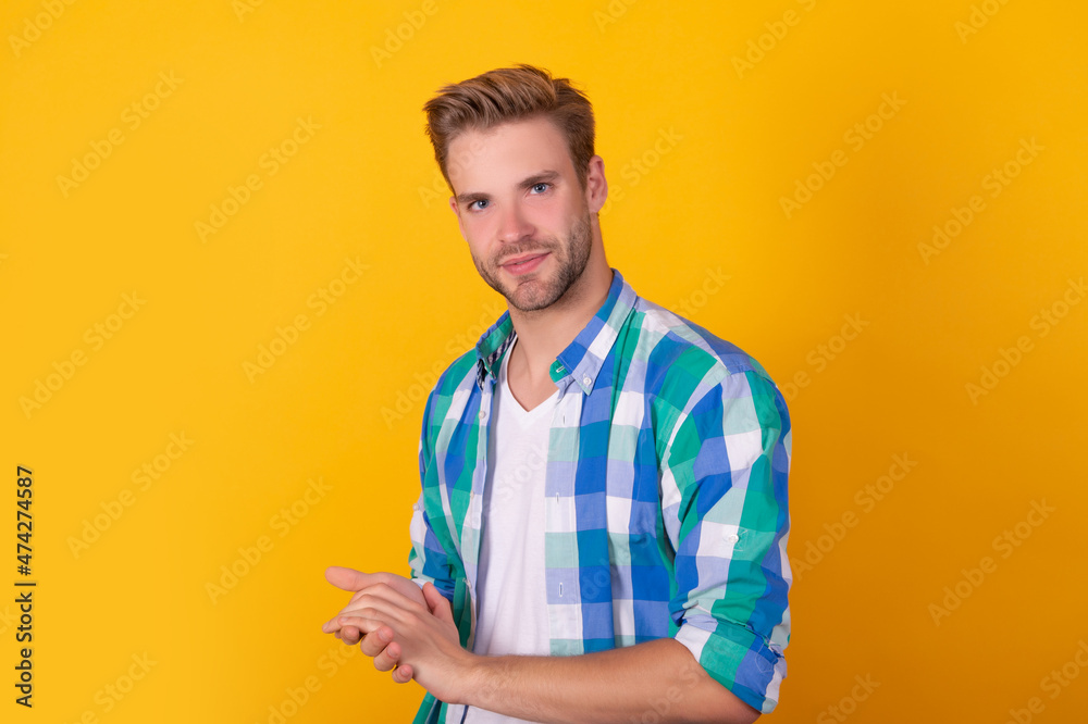 Handsome unshaven guy portrait keep hands together in checked shirt yellow background, serious