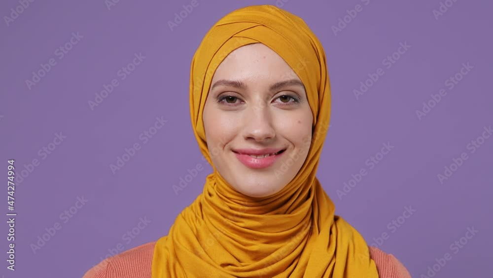 Close up young arabian asian muslim woman in abaya hijab yellow clothes look camera smiling isolated on plain pastel light violet background studio portrait. People uae middle eastern islam concept Close up young arabian asian muslim woman in abaya hijab yellow clothes look camera smiling isolated on plain pastel light violet background studio portrait. People uae middle eastern islam concept