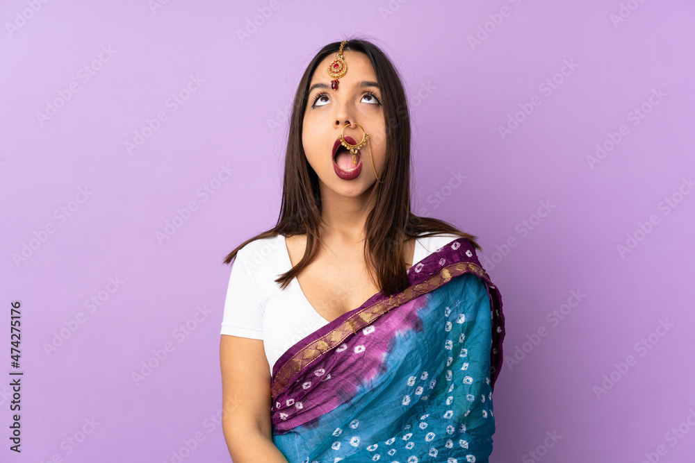 Young Indian woman isolated on purple background looking up and with surprised expression Young Indian woman isolated on purple background looking up and with surprised expression