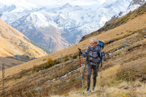 Teenager girl is hiking in the mountains. She has backpack, trekking poles, sunglasses. Golden autumn. Happy face.