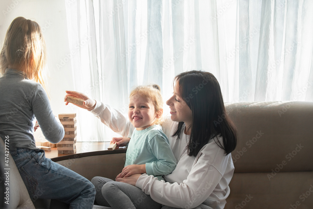 Three sisters of different ages play the board game , they lay out together wooden sticks together, in a cozy family environment Three sisters of different ages play the board game , they lay out together wooden sticks together, in a cozy family environment