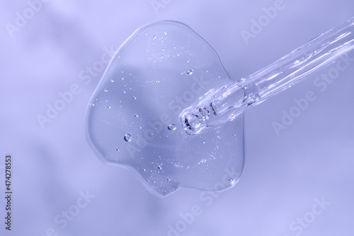 Pipette with fluid hyaluronic acid on violet blue background. Cosmetics and healthcare concept closeup. Dose of serum or retinol with air bubbles. Luxury gel or beauty product presentation in macro © Lavsketch