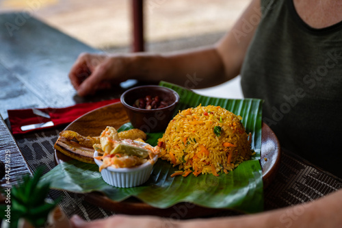 Traditional Costa Rican lunch of Gallo Pinto, rice and beans, with fried plantains, served on a wooden plate with palm leaf. photo