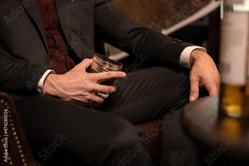 A rich man in an expensive suit sits in a dark room with a glass of whiskey. Alcohol in a glass close up