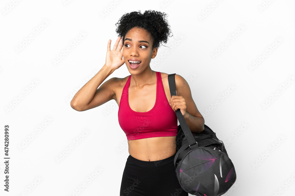 Young sport african american woman with sport bag isolated on blue background listening to something by putting hand on the ear