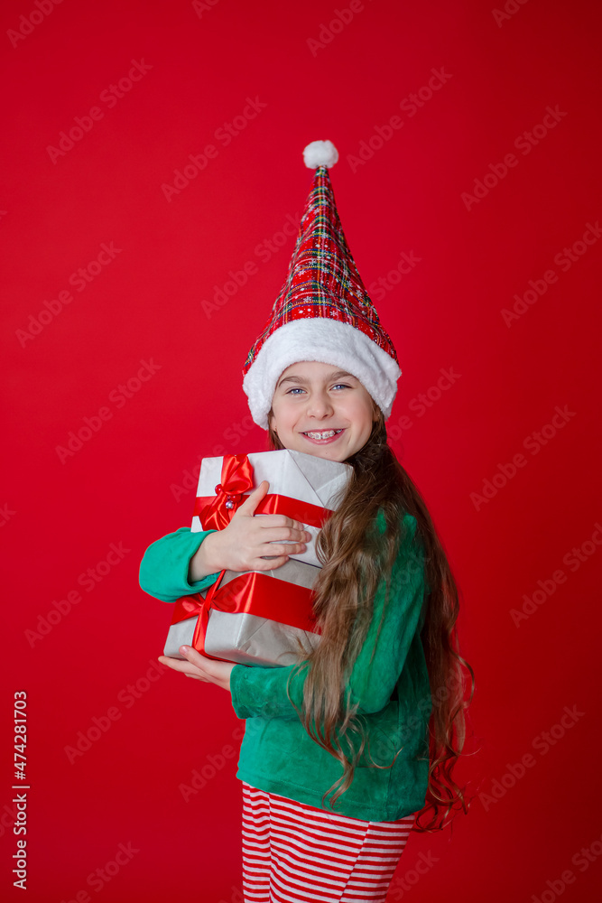Portrait of a joyful child with a gift. Elf girl with gifts, Santa Claus helper on a bright red bright colored background. Portrait of a joyful child with a gift. Elf girl with gifts, Santa Claus helper on a bright red bright colored background.