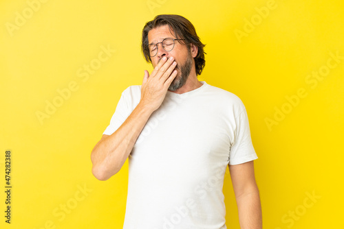 Senior dutch man isolated on yellow background yawning and covering wide open mouth with hand