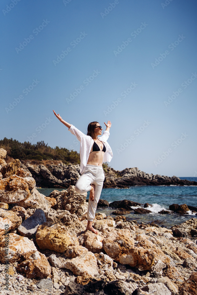Happy young woman enjoying freedom with open hands on vacation while standing on the coast rocks enjoying sea and blue sky view Happy young woman enjoying freedom with open hands on vacation while standing on the coast rocks enjoying sea and blue sky view