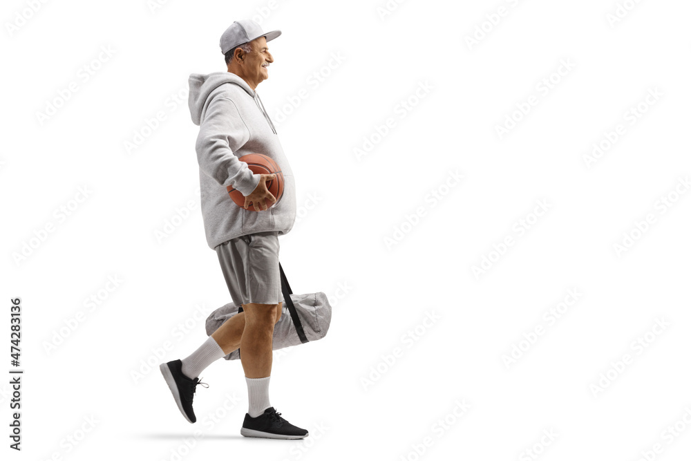 Full length profile shot of a mature man walking with a basketball and a sports bag Full length profile shot of a mature man walking with a basketball and a sports bag