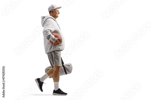 Full length profile shot of a mature man walking with a basketball and a sports bag