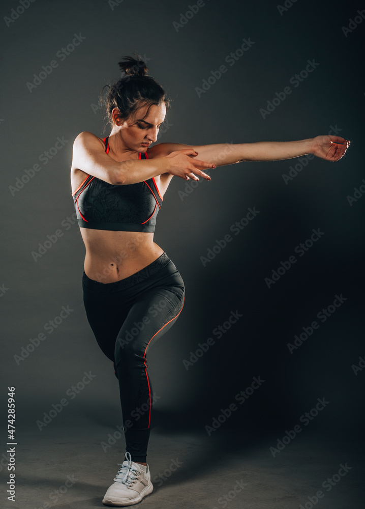 Flexible beautiful gymnast girl doing gymnastic exercises, doing stretching legs, on a dark background