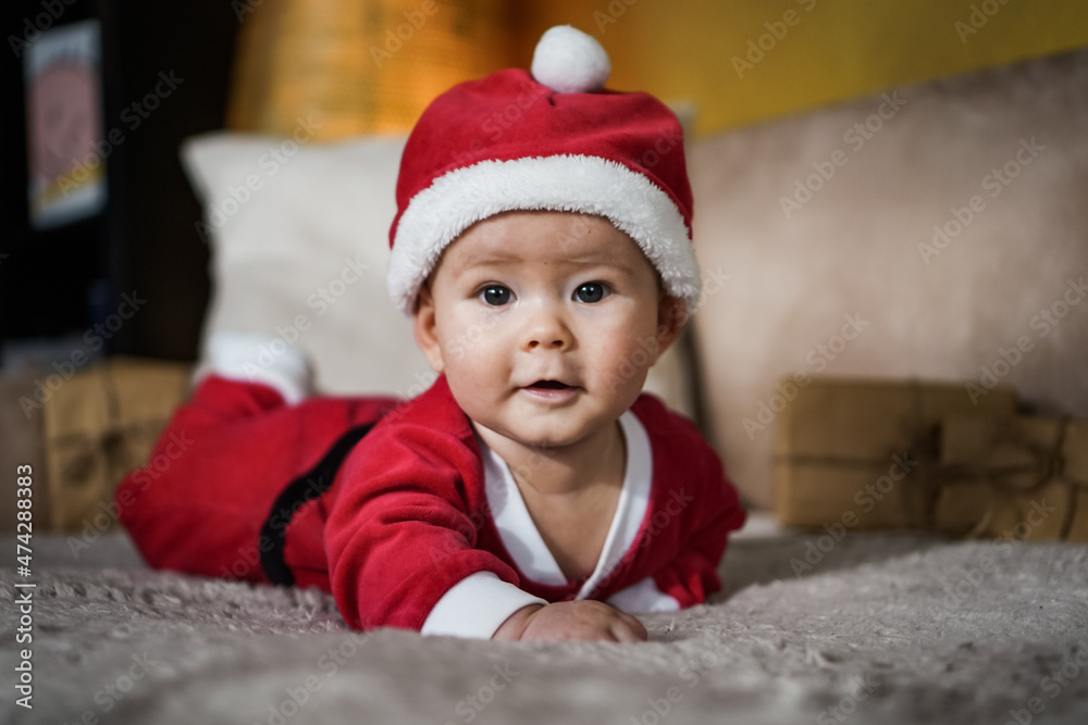 cute little newborn baby in christmas outfit with santa claus hat crawling on a couch in a cozy bright living room cute little newborn baby in christmas outfit with santa claus hat crawling on a couch in a cozy bright living room