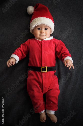 cute newborn baby in christmas outfit with santa claus hat lying on grey background for xmas