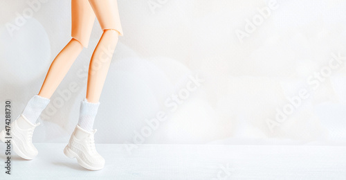 Legs of a doll in a white dress and shoes on a white background in the format of a banner