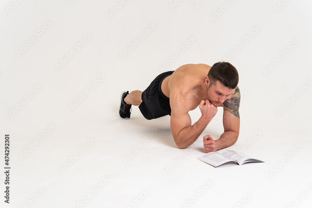 Bodybuilder reads the book on a white background isolated at the bottom of his head on his hands bodybuilder young muscle reader healthy, standing. manager biceps, posing tan Bodybuilder reads the book on a white background isolated at the bottom of his head on his hands bodybuilder young muscle reader healthy, standing. manager biceps, posing tan