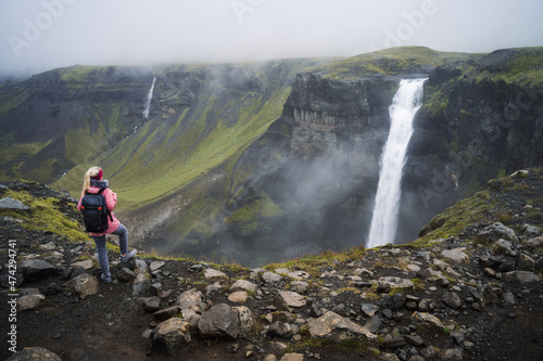 Woman with backpack and lilac jacket enjoying Haifoss waterfall of Iceland Highlands in Thjorsardalur Valley
