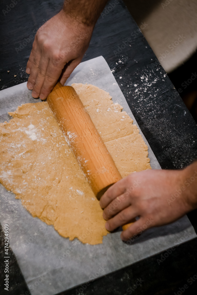 male hands roll gingerbread dough with a wooden rolling pin, close-up male hands roll gingerbread dough with a wooden rolling pin, close-up