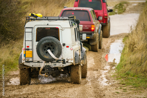 4x4 off-road vehicles driving across mud, water-logged terrain and wading through deep water pools, Wilts UK. Land Rover Discovery, Defender and Toyota 4Runner Hilux Surf © Martin