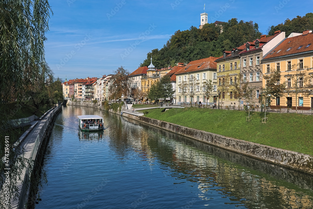 Ljubljana, Slovenia. Historical buildings along the Ljubljanica River and Castle Hill with lookout tower of Ljubljana Castle in sunny autumn day. View from the St. James's Bridge across the river.