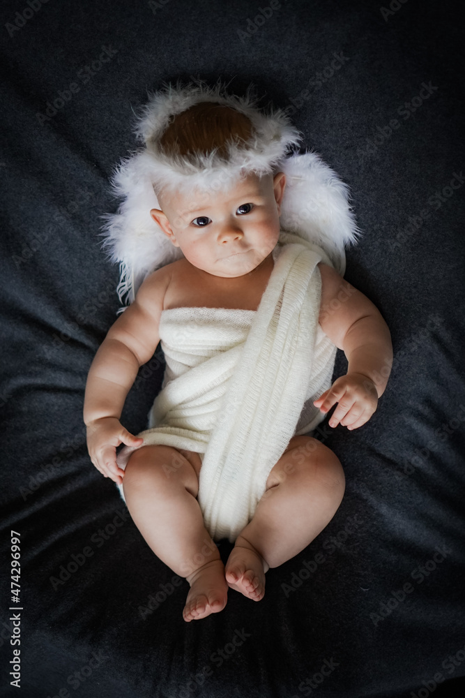 cute happy innocent newborn baby in white angel outfit with feather wings lying on a grey background symbolizes safety and freedom cute happy innocent newborn baby in white angel outfit with feather wings lying on a grey background symbolizes safety and freedom