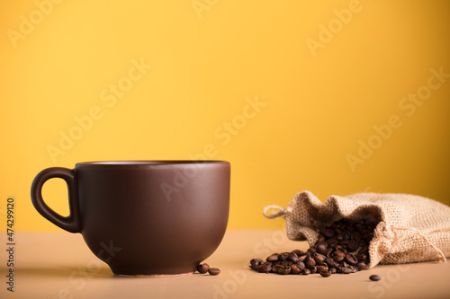 brown cup with coffee and raffia sack with roasted coffee beans, with yellow background