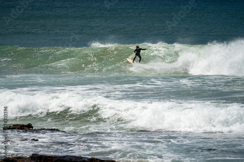 male surfer catching waves surfing at south coast beach on a bright warm sunny day on clear blue water