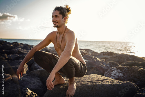 Yoga teacher is practicing on the rocks, sunset time. Man exercising, stretching body. Pranayama. Mindfulness. Meditation.
