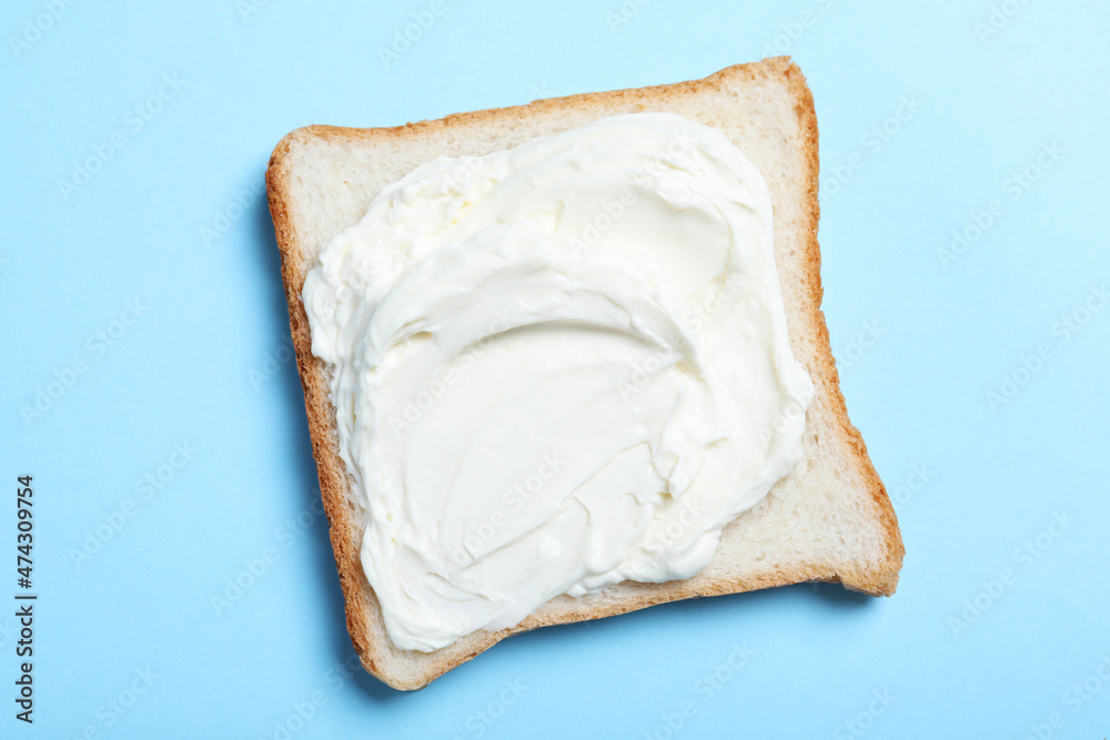 Slice of bread with tasty cream cheese on light blue background, top view