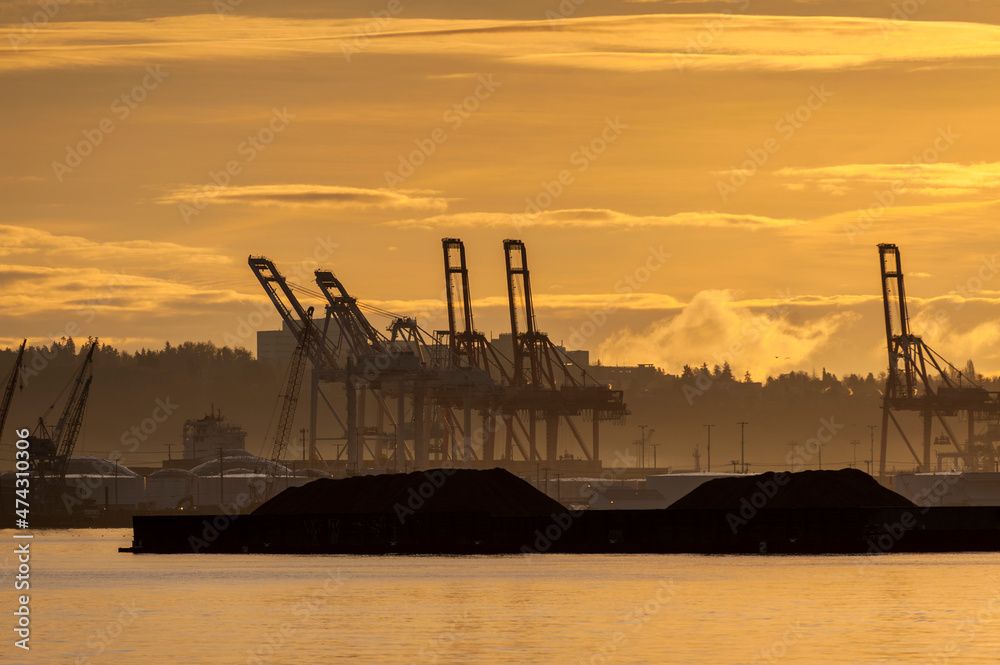 Fototapeta premium Sunrise on Elliott Bay with Silhouetted Seattle Dockyard Cranes. Waterfront with cranes for loading shipping containers onto container ships.