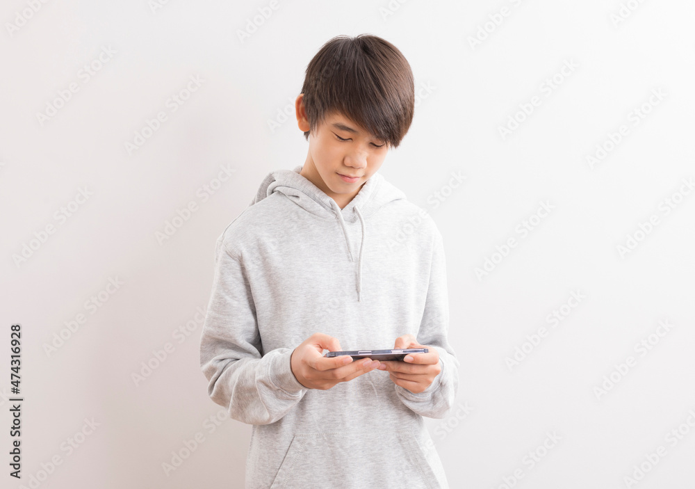 Asian teen boy schooler texting or playing game online on smartphone isolate on white background. Asian teen boy schooler texting or playing game online on smartphone isolate on white background.