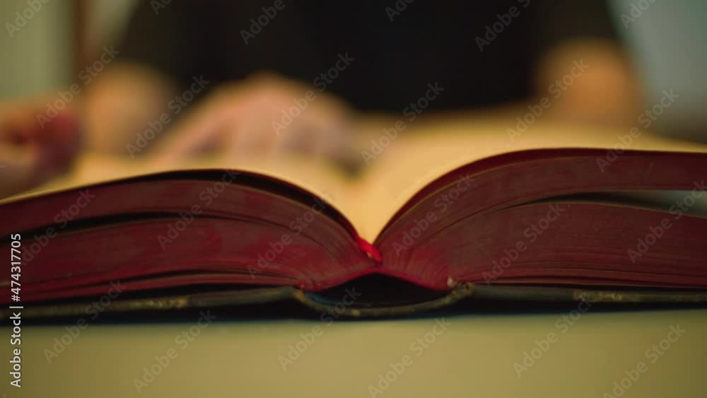 Close up view of a student reading a red old book and turning pages slowly. Concept of ancient writings, library, learning, to study, literature in a vintage style.