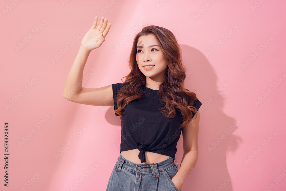 Young woman covering face by hand of bright light looking at camera on pink background Young woman covering face by hand of bright light looking at camera on pink background