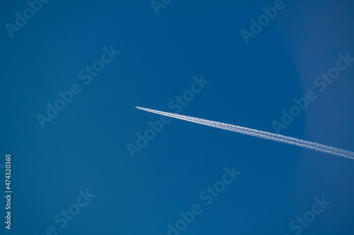 Jet airpllane with thick trace flies to the sun in deep blue sky